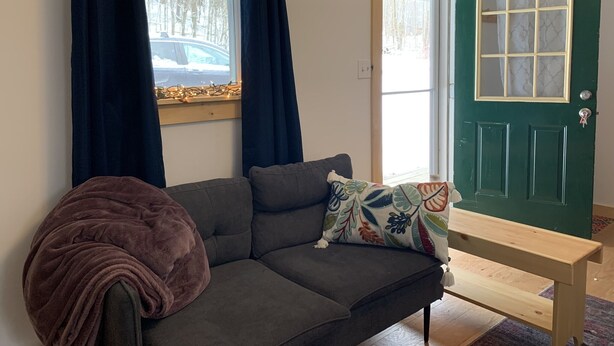 A cozy room with a grey sofa, a bench, and a green door with frosted glass panels. - New York Vermont Border Cottage Getaway (Granville)
