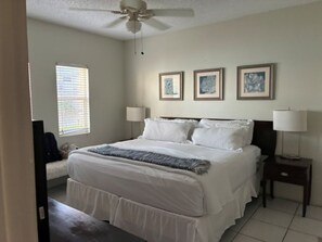 Ein Schlafzimmer mit einem Bett, zwei Nachttischen, einem Deckenventilator und drei gerahmten Bildern an der Wand.