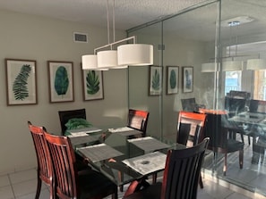 Un espace repas moderne avec une table en verre entourée de chaises, des reproductions botaniques encadrées accrochées au mur et un luminaire suspendu.