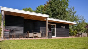 Un edificio moderno con facciata scura, una zona relax esterna coperta e un ingresso ben visibile.
