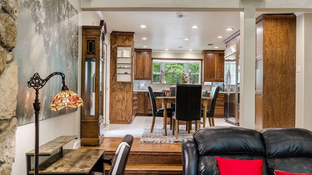 A spacious living area with a wooden dining table, a black leather sofa with a red pillow, and a stained glass lamp.