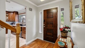 A hallway with a wooden door, a kitchen area, and a dining table with a basket of flowers.