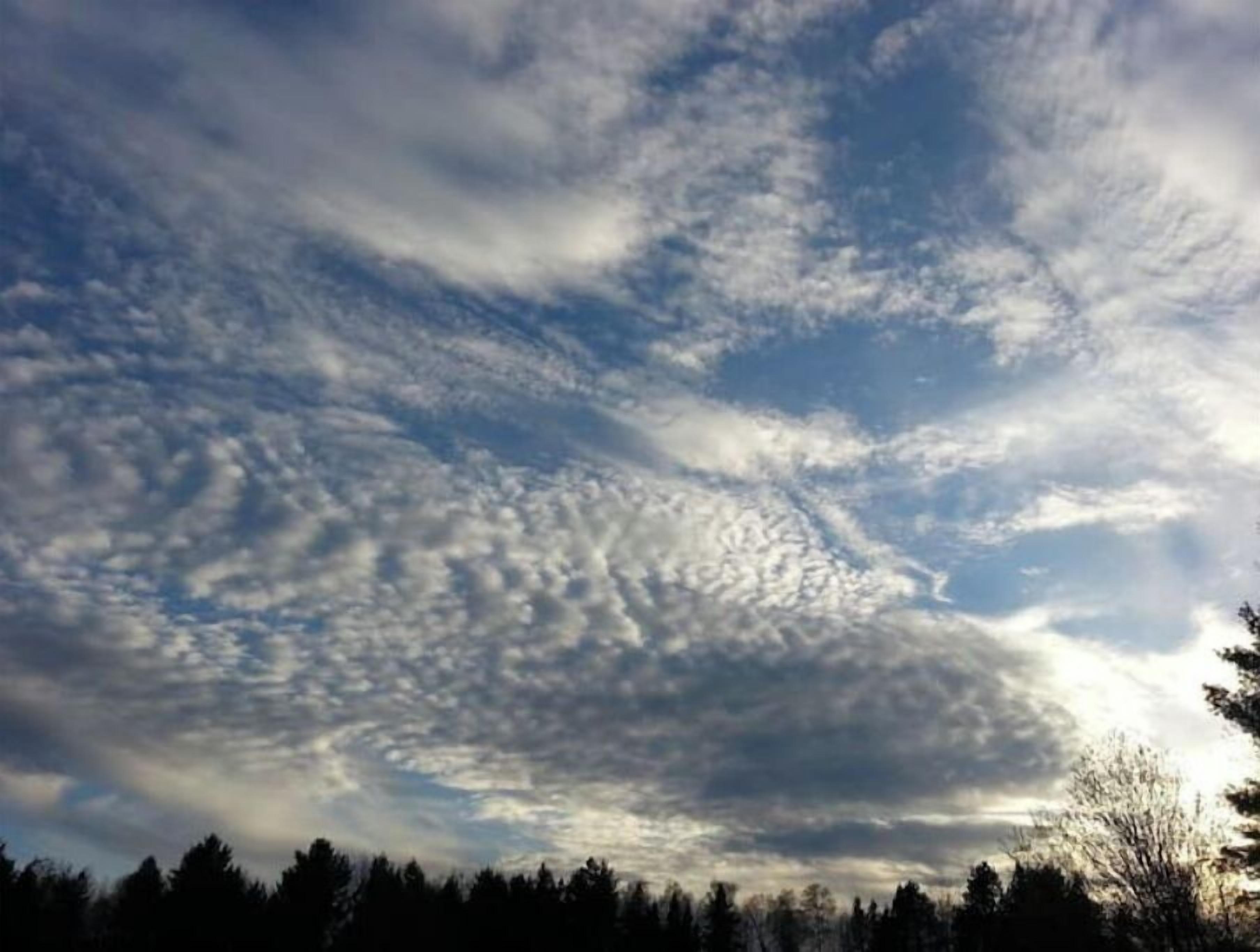 A clear sky with scattered clouds and a forested area below.