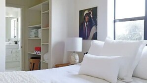 A hotel room with a neatly made bed, a white wardrobe, and a painting on the wall.