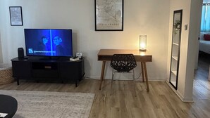 Una sala de estar con televisor, un mapa enmarcado, un escritorio de madera, una silla y una mesita con lámpara.