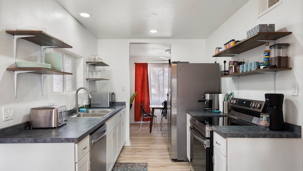 Una cocina moderna con electrodomésticos de acero inoxidable, estantes de madera y vista al área de comedor.