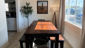 Un comedor con mesa de madera, sillas, ventilador de techo, un cuadro enmarcado, lámpara y ventana con vistas.