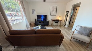 Una sala de estar con un sofá marrón, un televisor, un escritorio y una silla.