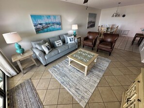 A living room with a grey sofa, two brown leather armchairs, a coffee table, and a painting of a marina.