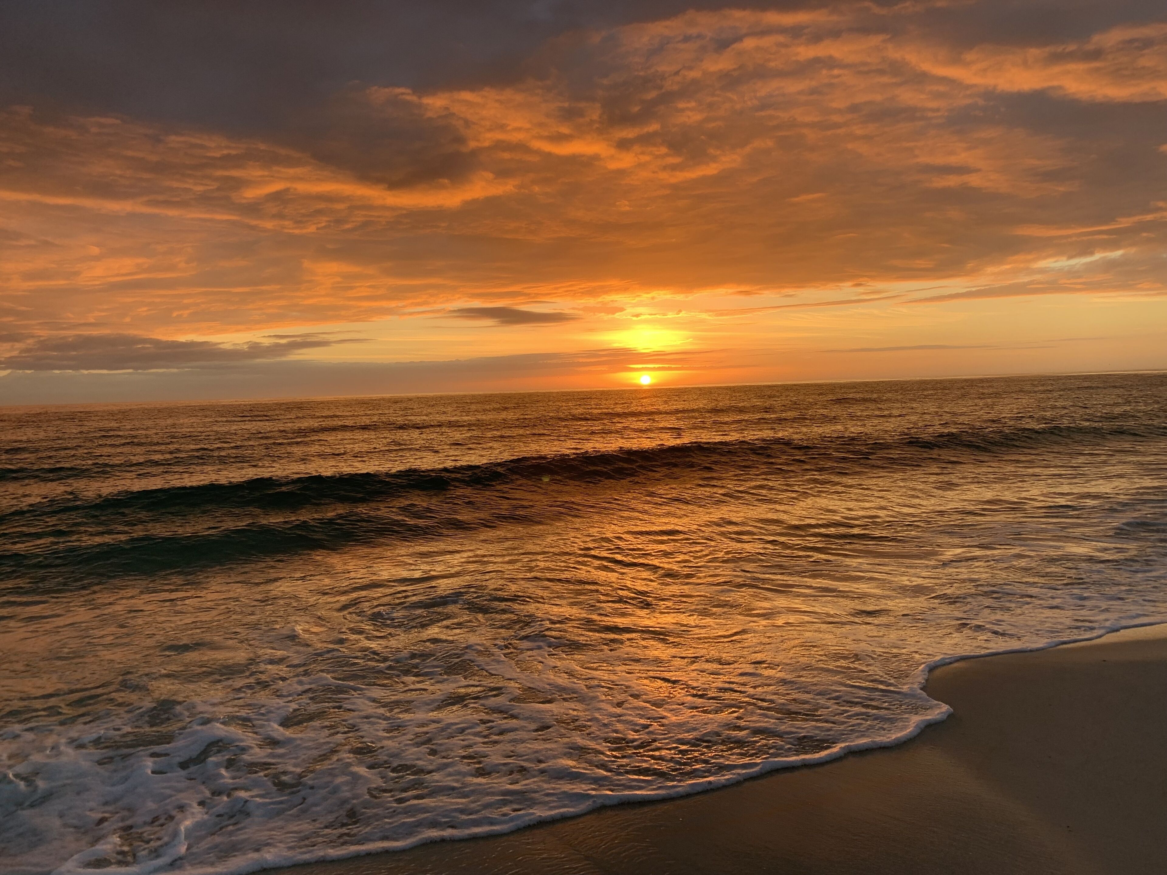 A beach with waves and a sunset.