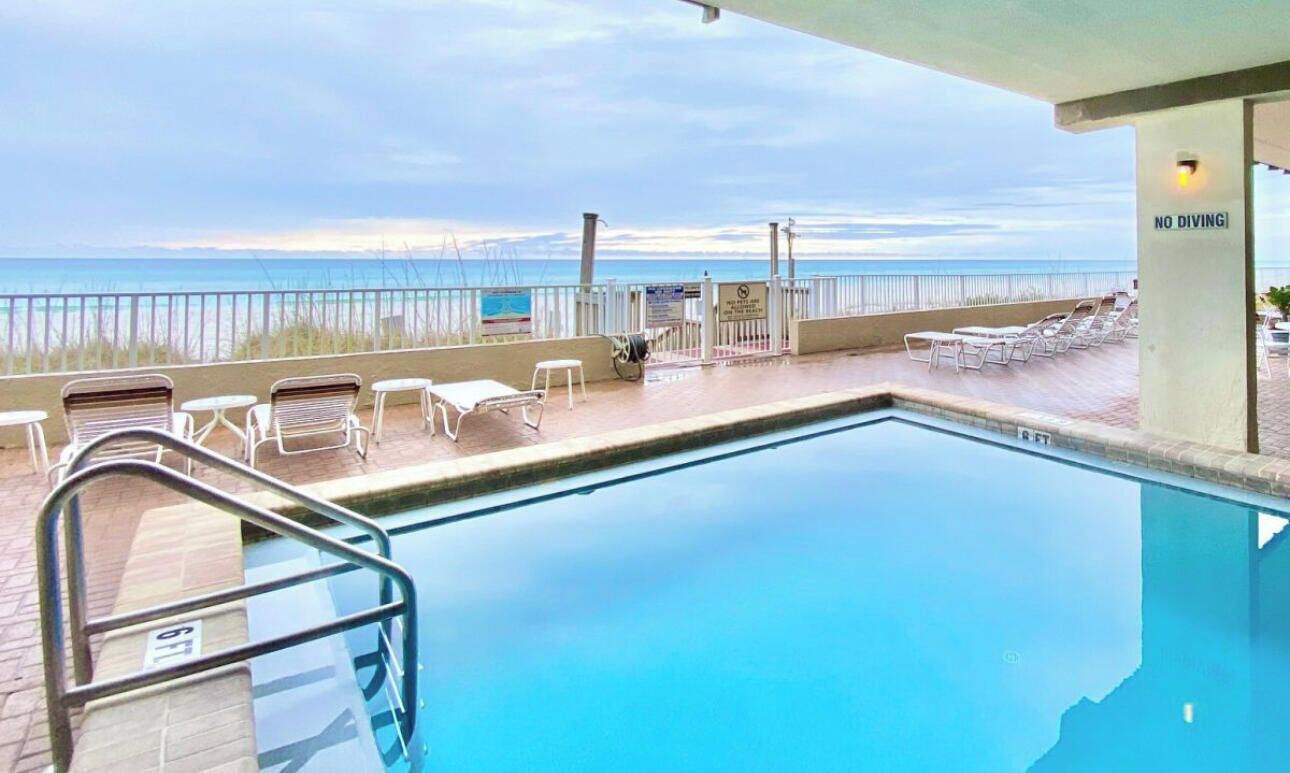 A pool area with a view of the beach, lounge chairs, and a 'No Diving' sign.