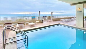 Área da piscina com vista para a praia, cadeiras de descanso e placa de 'Não Mergulhar'.