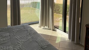 Quarto com uma cama grande, vista do oceano através de uma porta de vidro deslizante e varanda com cortinas.