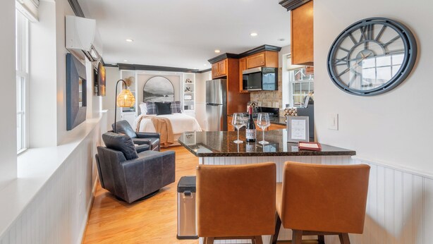 A modern kitchen with a central island, wooden cabinets, and a large clock on the wall. - Cozy Loft for 2- Steps from Village of Pittsford (Pittsford)