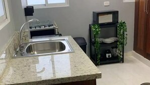 Una cocina con encimera de granito, pileta de acero inoxidable y un pequeño comedor con mesa de vidrio y un tazón.