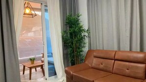 Un salón con un sofá de cuero marrón, una mesa de madera con una planta y vistas a través de un ventanal.