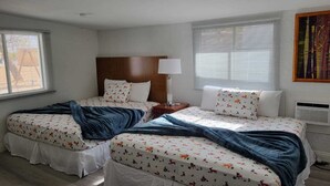 A bedroom with two beds, each with a patterned bedspread, a bedside table with a lamp, and a window with blinds. - Family Ranch in pahrump (Pahrump)