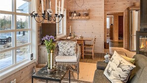 Ein gemütliches Blockhaus-Interieur mit Essbereich, Kamin und großem Fenster mit Blick auf eine verschneite Landschaft.