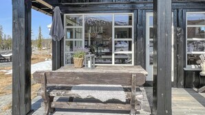 Eine Holzhütte mit großen Fenstern, einer Bank und einem Blumenkorb auf der Veranda.