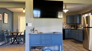 Una cocina moderna con un televisor de pantalla plana, armarios azules y una mesa de comedor de madera con sillas.