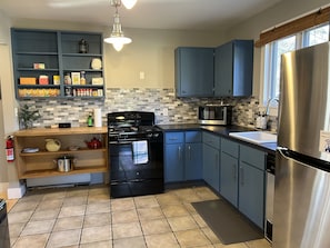 Eine moderne Küche mit einem schwarzen Herd, blauen Schränken, einem Edelstahl-Kühlschrank und einer gefliesten Spritzschutzwand.
