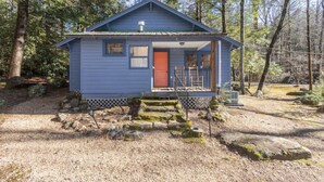 A small, single-story cabin with a red door, surrounded by trees and a gravel driveway. - Ole Blue - Table Rock, Sassafras, Lake Keowee, Lake Jocassee. (Sunset)
