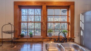 A kitchen with a large window, wooden cabinetry, a double sink, and a metal rack. - Ole Blue - Table Rock, Sassafras, Lake Keowee, Lake Jocassee. (Sunset)