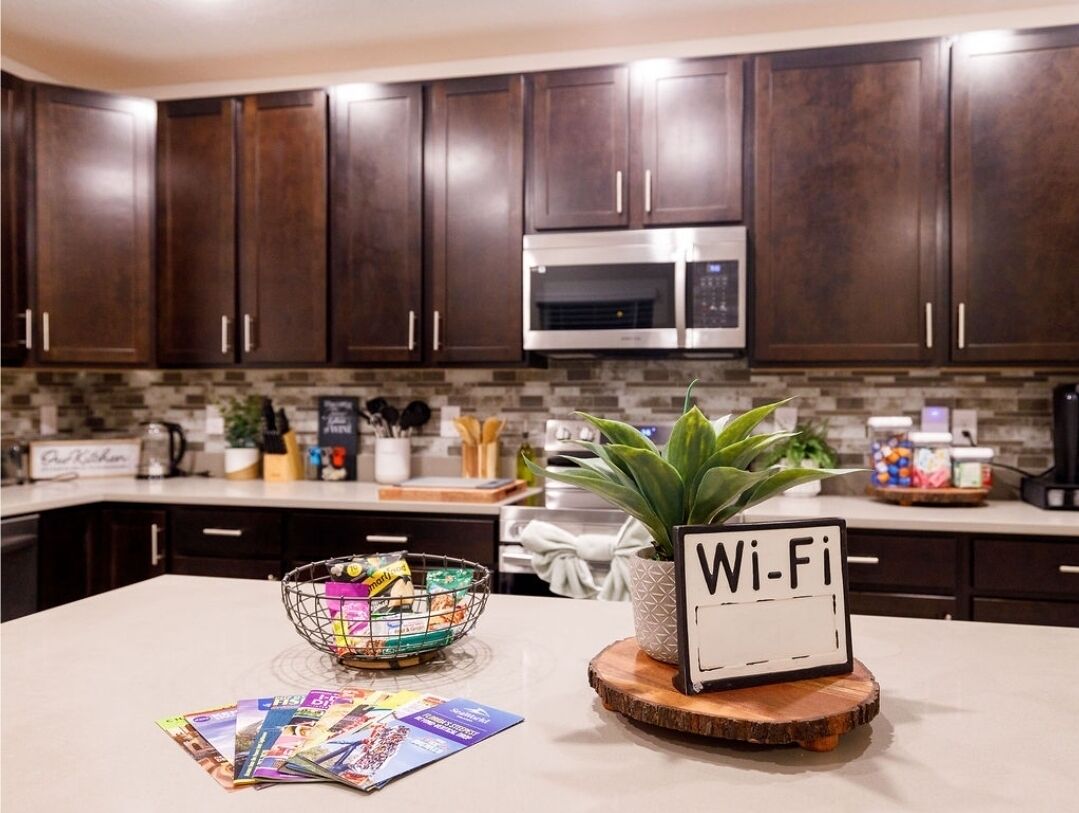 A kitchen with dark wood cabinets, a stainless steel microwave, a Wi-Fi sign, a bowl with snacks, and a potted plant.