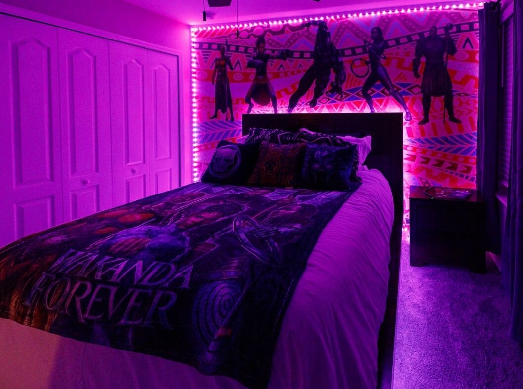 A bedroom with a bed, a headboard with a poster, and a wall with silhouettes.