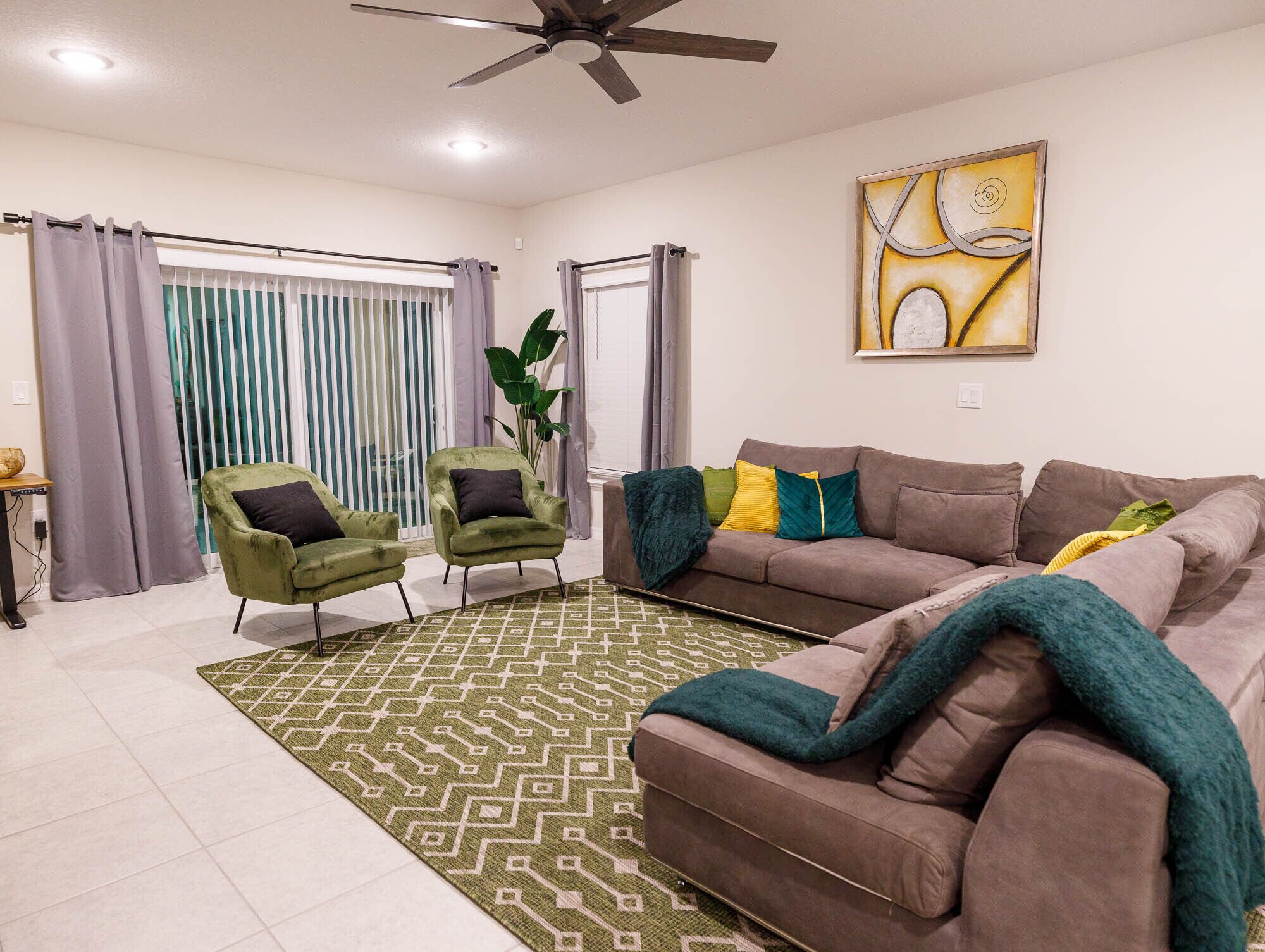 A living room with a brown sofa, two green armchairs, a patterned rug, and a ceiling fan.