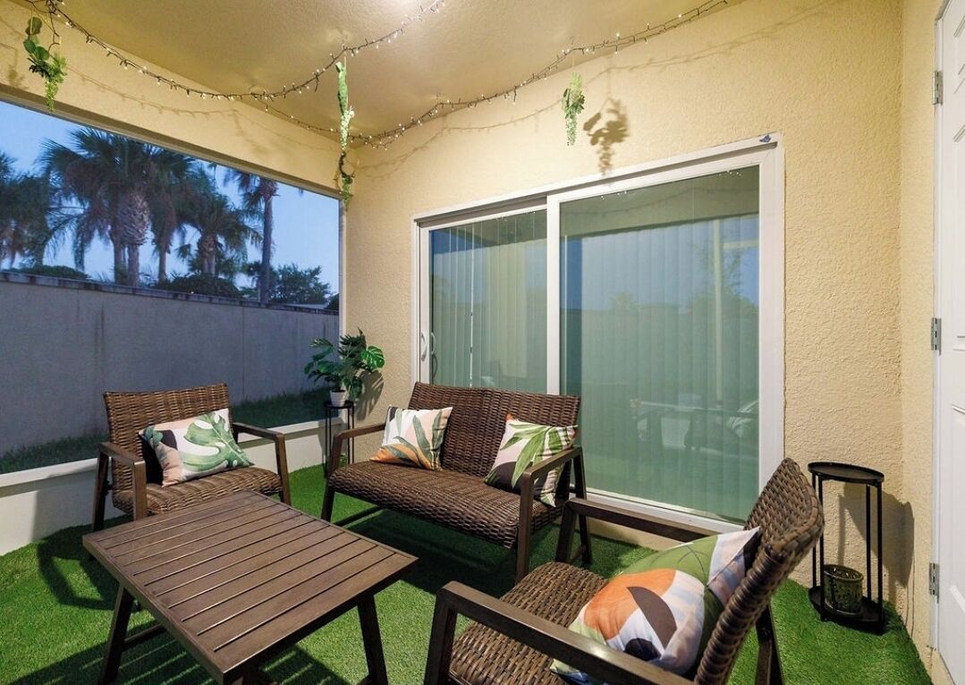 Une terrasse extérieure avec une table et deux canapés en osier, une plante en pot et une porte-fenêtre coulissante.