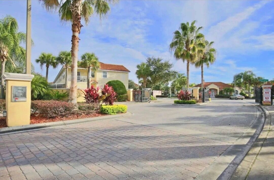 A residential street with houses, palm trees, and a paved road.