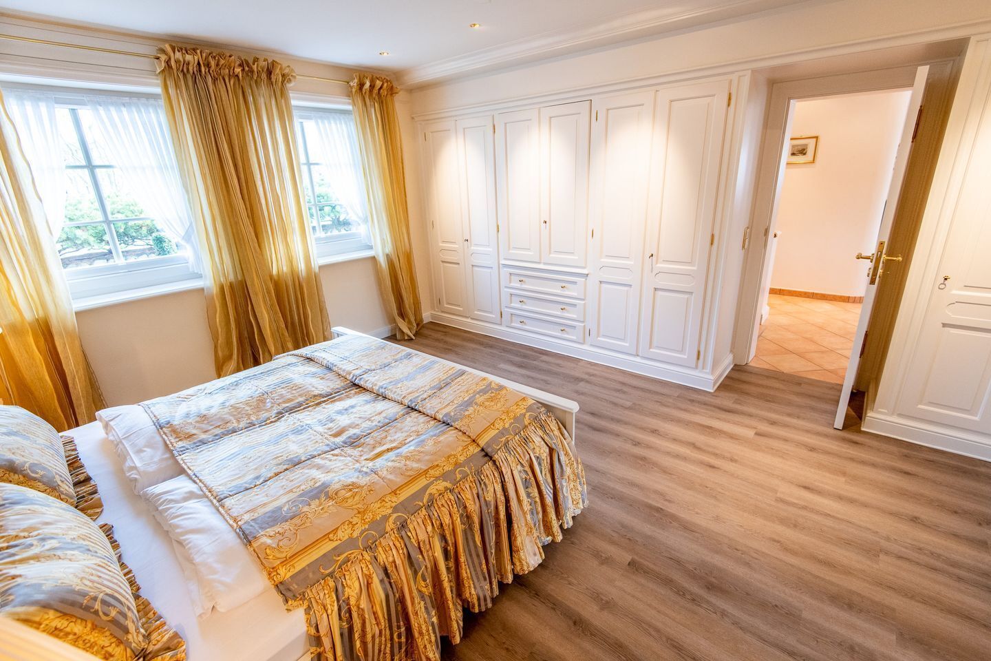A spacious bedroom with a large bed, a wardrobe, and a door leading to another room.