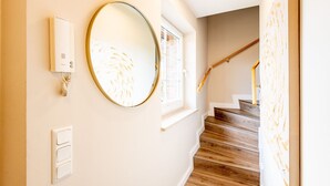 Un couloir avec un escalier en bois, un miroir rond et un luminaire fixé au mur.