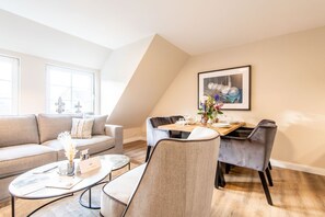 Een moderne woonkamer met een bank, salontafel en een eetgedeelte met stoelen en een tafel gedekt voor een maaltijd.
