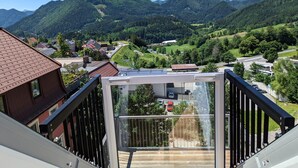 A balcony with a glass enclosure overlooking a mountainous landscape with houses and greenery. - Apartment in Mariazell Near Ski Slopes (Mariazell)