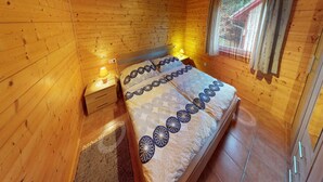 Camera da letto in una baita di legno, con un letto, comodini e una finestra con tende.