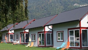 Una serie di casette basse con ampie finestre e rivestimenti rossi, immerse in una zona erbosa con montagne boscose sullo sfondo.