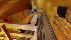 Un accogliente interno di una baita in legno con un divano, una televisione e un angolo cottura.