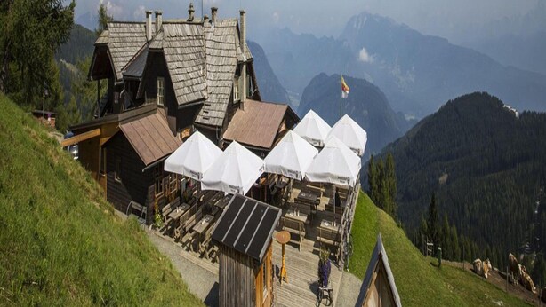 Un rifugio alpino rustico con strutture in legno e una sala da pranzo con ombrelloni bianchi.