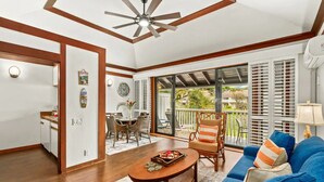 A spacious living area with a ceiling fan, a dining table with chairs, a blue sofa, and a balcony with white shutters. - NEW! Top Floor Views with A/C in Poipu Beach, Resort Amenities (Koloa)