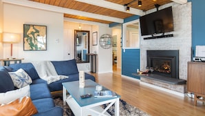 Ein modernes Wohnzimmer mit einem blauen Sofa, einem Couchtisch, einem Kamin und einem an einer Ziegelwand befestigten Fernseher.