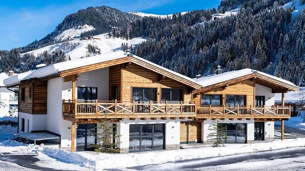 A modern chalet with a wooden balcony, large windows, and a snowy mountain backdrop. - Spacious Family Flat in Kleinarl (Kleinarl)
