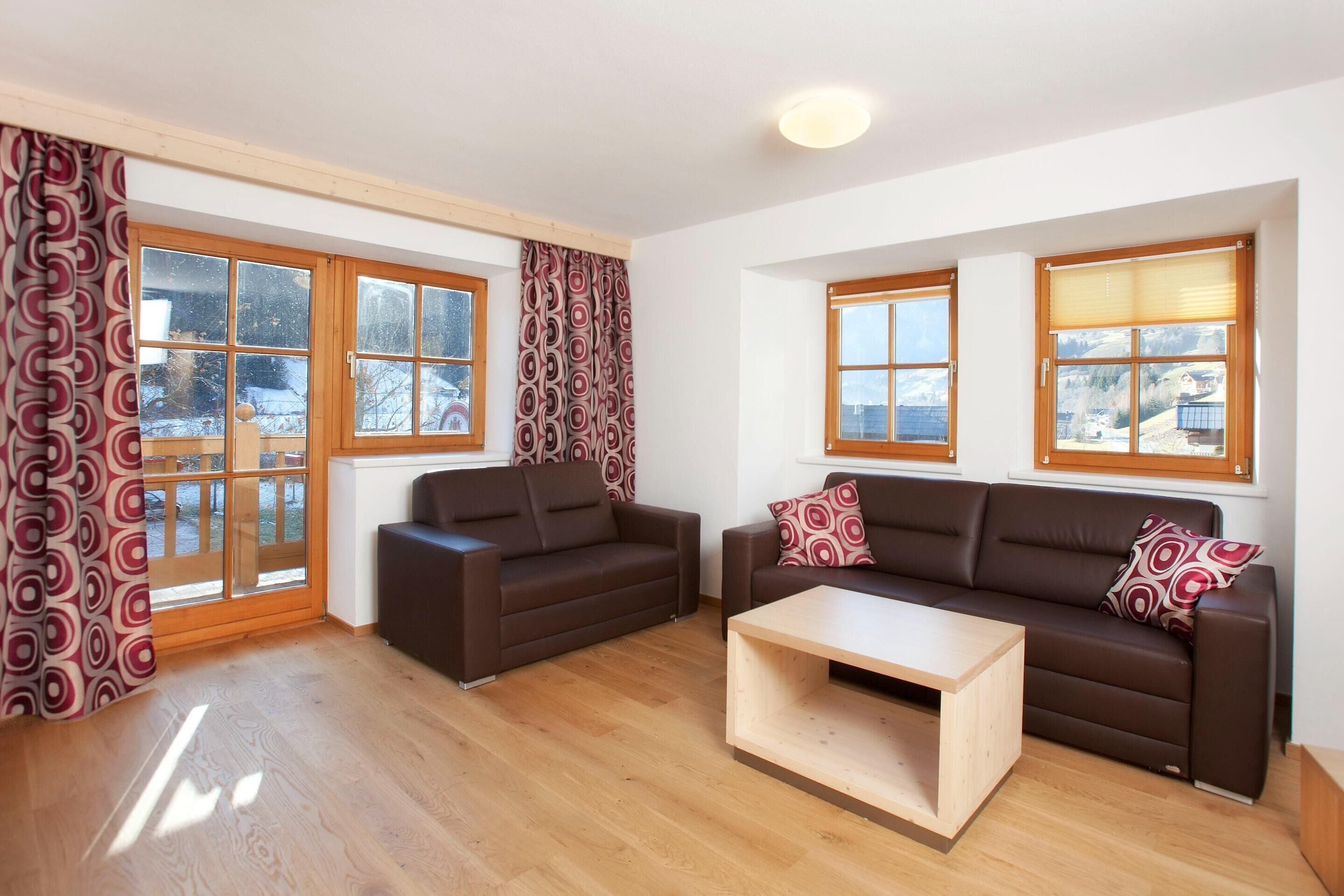 A living room with two sofas, a coffee table, and large windows with curtains.