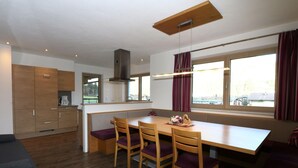 A modern kitchen with wooden cabinets, a dining table with four chairs, and a large window with curtains. - Chalet in Kaltenbach Near Ski Lift (Kaltenbach)