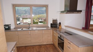 A modern kitchen with wooden cabinets, a stainless steel sink, a microwave, and a view of a town through a large window. - Chalet in Kaltenbach Near Ski Lift (Kaltenbach)