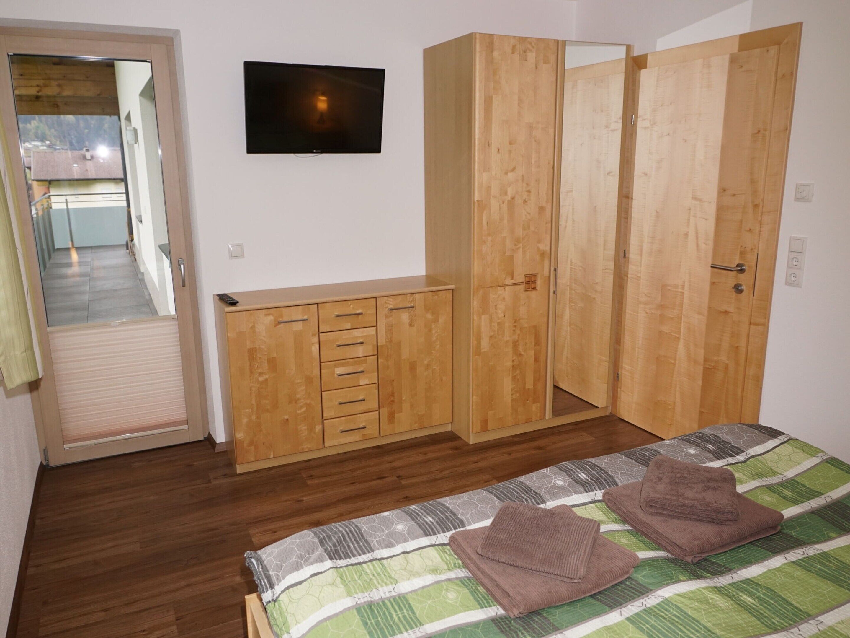 Quarto com cama, guarda-roupa de madeira e televisão na parede.