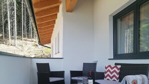 A balcony with wicker furniture, a glass table, and a window with a view of trees. - Contemporary Apartment in Gerlosberg Near Forest (Gerlosberg)