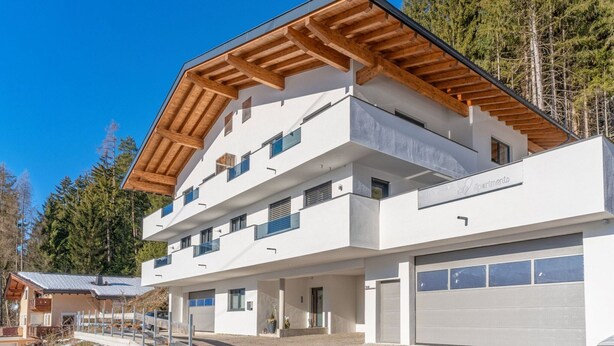 A modern multi-story building with a flat roof, wooden beams, and a white facade. - Contemporary Apartment in Gerlosberg Near Forest (Gerlosberg)