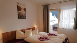 A bedroom with a wooden bed, two pillows, a purple bedspread, and a window with a view of a snowy landscape. - Contemporary Apartment in Gerlosberg Near Forest (Gerlosberg)